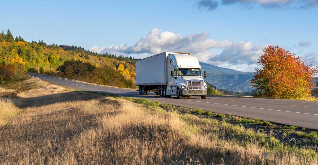 White tractor trailer traveling a rural autumn road